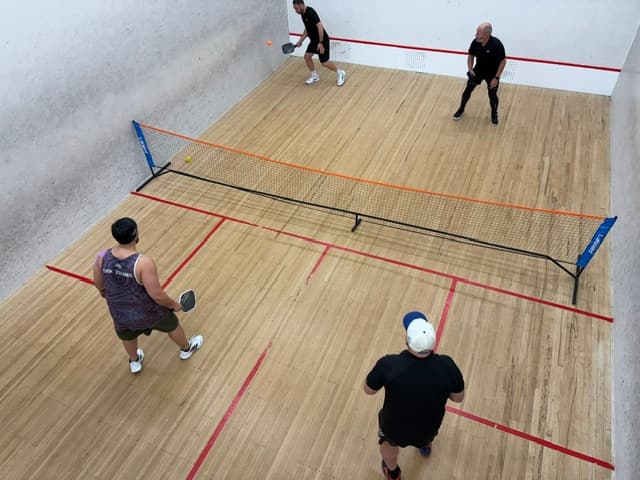 A group playing pickleball on an indoor squash court