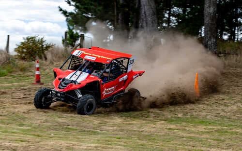 A red Polaris off-road vehicle racing around a dirt course